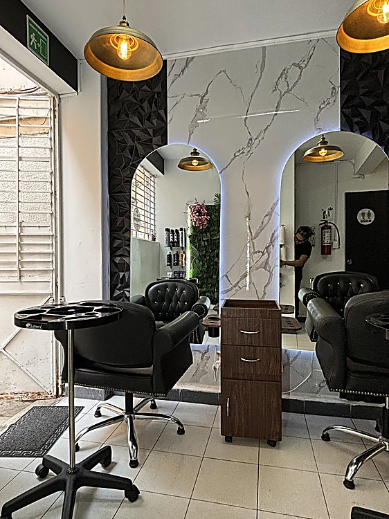 Interior del salón: dos espejos en arco con luz blanca, muro de mármol, lámparas doradas y sillas negras